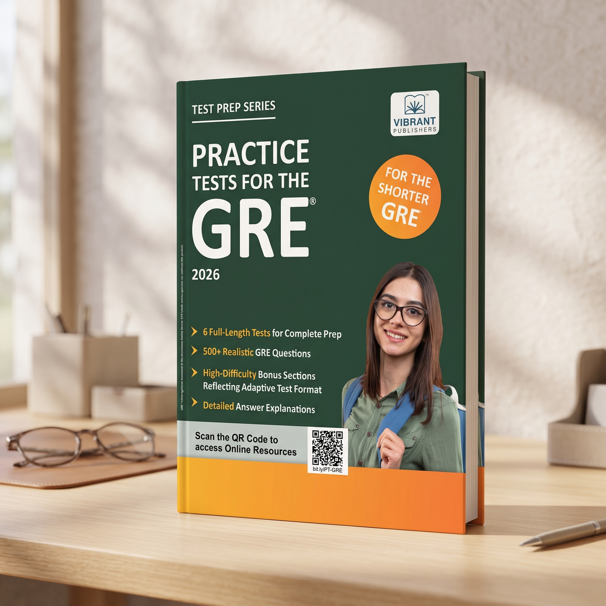 A paperback GRE practice test book titled 'Practice Tests for the GRE 2026' stands open on a wooden desk in a softly lit room. 